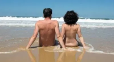 A couple sitting nude on the beach in the water